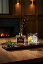 Load image into Gallery viewer, A reed diffuser bottle with a clear glass square base, a black label reading 'BOUGIE Juniper House', and multiple black reed sticks extending upward through a gold collar, on a light gray background.