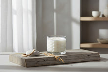 Load image into Gallery viewer, A white wax candle in a clear textured glass jar with a faceted base, photographed against a light gray studio background.