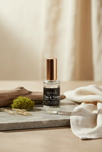 Load image into Gallery viewer, A bottle of BOUGIE Tide & Timber room spray with a metallic rose gold cap, styled on a gray stone slab with dried wheat, moss, and a beige linen cloth.