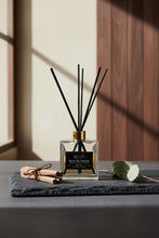Load image into Gallery viewer, A clear glass reed diffuser bottle with black diffuser sticks and a gold collar, featuring a black label with white text that reads 'BOUGIE Bois de Santal'.
