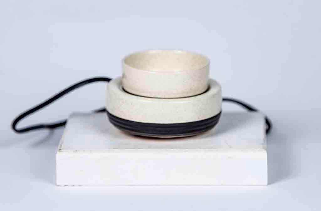 Stack of ceramic candle warming bowls on a white block with a light gray background