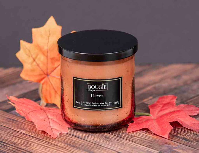 Candle labeled 'Bougie Napa Harvest' with autumn leaves on a wooden surface