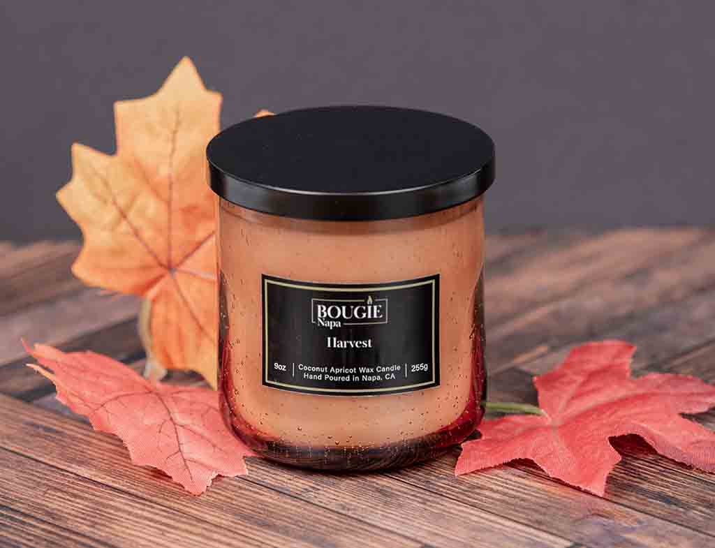 Candle labeled 'Bougie Napa Harvest' with autumn leaves on a wooden surface