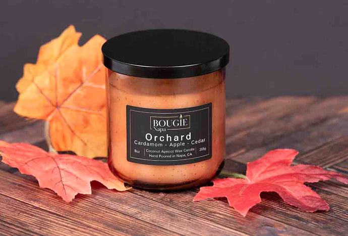 Candle jar labeled 'Orchard' with autumn leaves on a wooden surface