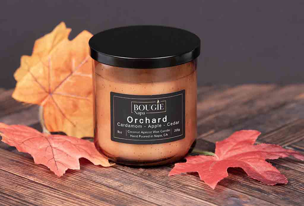 Candle jar labeled 'Orchard' with autumn leaves on a wooden surface