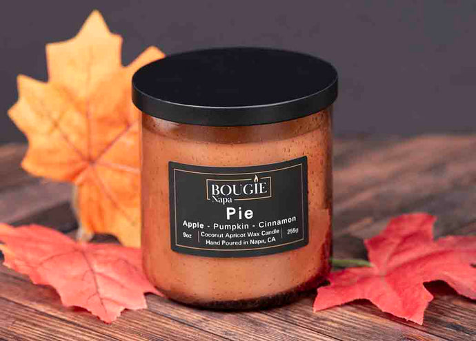 Candle labeled 'Pie' with autumn leaves on a wooden surface