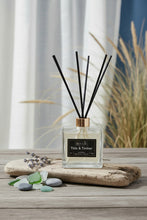 Load image into Gallery viewer, A reed diffuser bottle with a clear glass square base, a black label reading 'Bougie Tide &amp; Timber', and multiple black reed sticks extending upward through a gold collar, on a light gray background.
